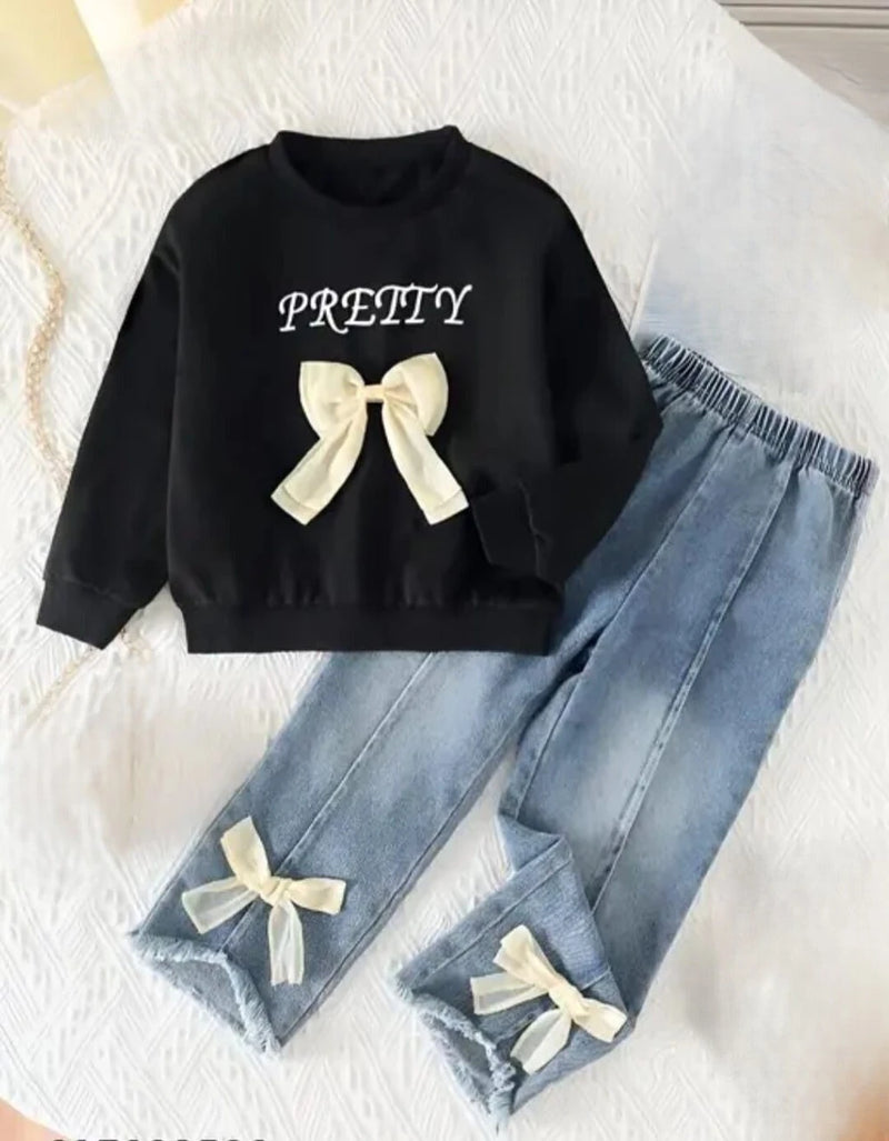 A children's two-piece outfit set featuring a black sweatshirt with 'PRETTY' text and a cream bow, paired with light blue denim pants with elastic cuffs and cream bow details.