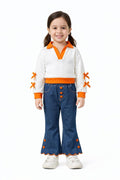 A young girl with dark hair in pigtails stands against a white background wearing a white ribbed knit sweater with bright orange collar, hem, cuffs, and sleeve accents, paired with blue flared jeans featuring orange button details and hem trim, and white sneakers.